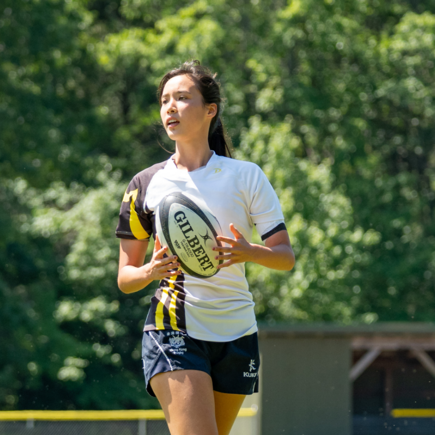 A young woman jogging and carrying a rugby ball